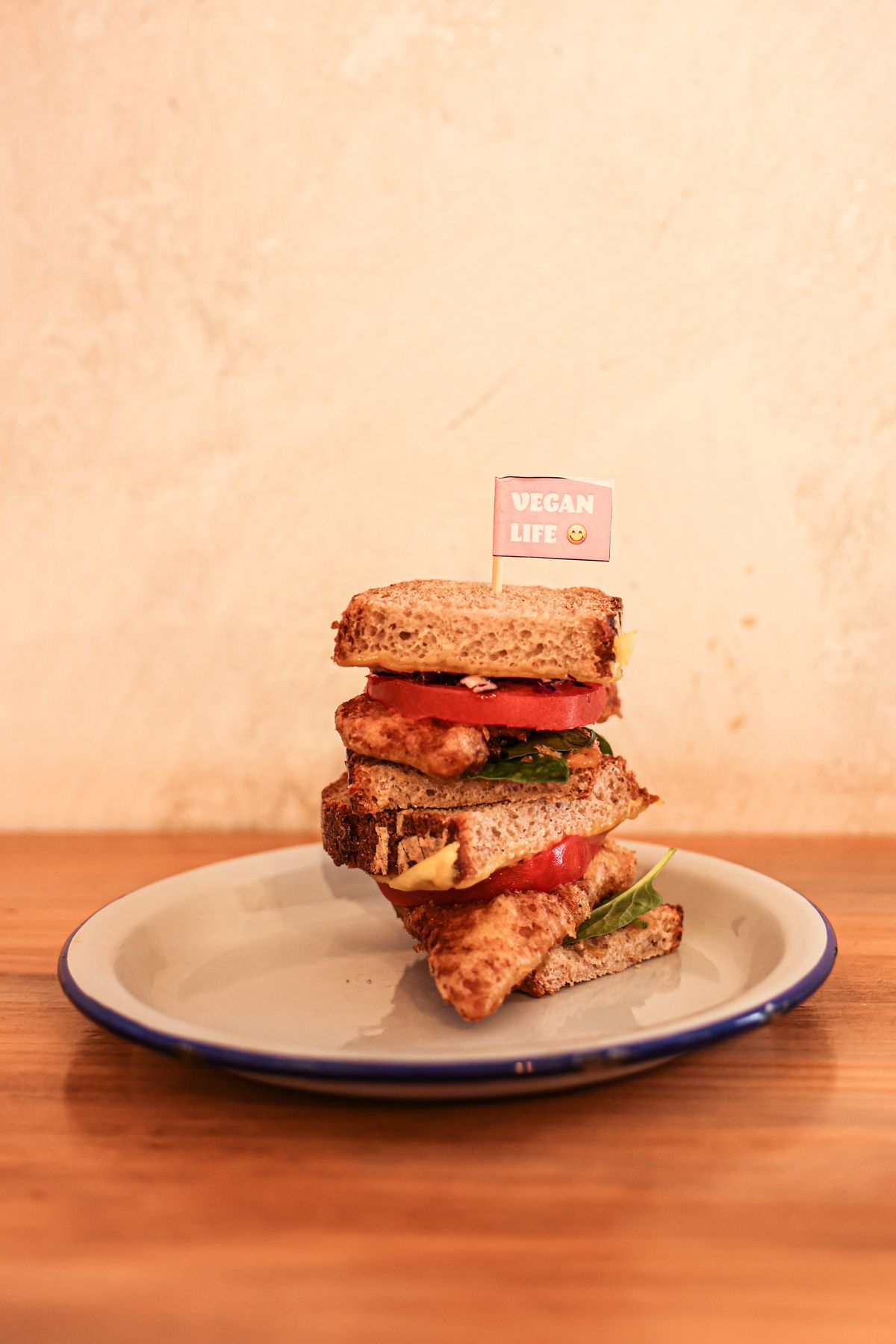 A stacked plant-based sandwich with tomato and greens on a plate